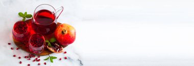 bir sürahi taze hazırlanmış nar suyu ve mermer bir tablo ve nane yaprakları ve meyve tohumları ile arka planı gri taş iki bardak