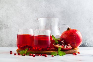 bir sürahi taze hazırlanmış nar suyu ve mermer bir tablo ve nane yaprakları ve meyve tohumları ile arka planı gri taş iki bardak