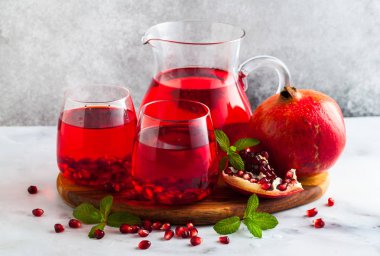 bir sürahi taze hazırlanmış nar suyu ve mermer bir tablo ve nane yaprakları ve meyve tohumları ile arka planı gri taş iki bardak