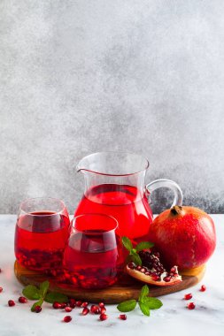 bir sürahi taze hazırlanmış nar suyu ve mermer bir tablo ve nane yaprakları ve meyve tohumları ile arka planı gri taş iki bardak
