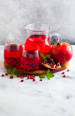 bir sürahi taze hazırlanmış nar suyu ve mermer bir tablo ve nane yaprakları ve meyve tohumları ile arka planı gri taş iki bardak