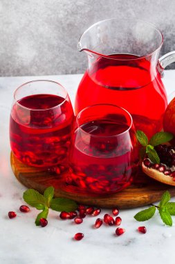 bir sürahi taze hazırlanmış nar suyu ve mermer bir tablo ve nane yaprakları ve meyve tohumları ile arka planı gri taş iki bardak