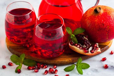 bir sürahi taze hazırlanmış nar suyu ve mermer bir tablo ve nane yaprakları ve meyve tohumları ile arka planı gri taş iki bardak