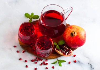 bir sürahi taze hazırlanmış nar suyu ve mermer bir tablo ve nane yaprakları ve meyve tohumları ile arka planı gri taş iki bardak