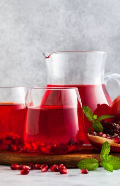 bir sürahi taze hazırlanmış nar suyu ve mermer bir tablo ve nane yaprakları ve meyve tohumları ile arka planı gri taş iki bardak