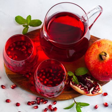 bir sürahi taze hazırlanmış nar suyu ve mermer bir tablo ve nane yaprakları ve meyve tohumları ile arka planı gri taş iki bardak