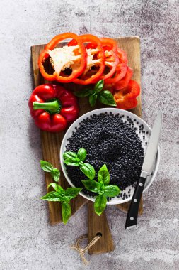 kırmızı, Olgun, dolmalık biber bir kesme tahtası ve taze fesleğen yaprakları kesti. Siyah mercimek ve bıçak. Arka plan gri taş yemek pişirme 