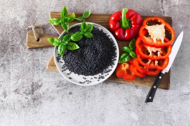 kırmızı, Olgun, dolmalık biber bir kesme tahtası ve taze fesleğen yaprakları kesti. Siyah mercimek ve bıçak. Arka plan gri taş yemek pişirme 