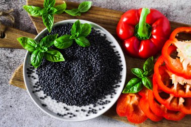 kırmızı, Olgun, dolmalık biber bir kesme tahtası ve taze fesleğen yaprakları kesti. Siyah mercimek. Arka plan gri taş yemek pişirme 