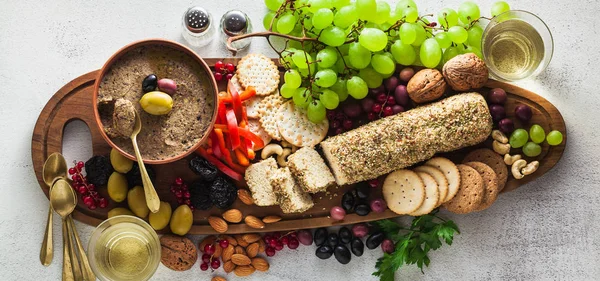 banner of Wooden serving board with vegan snacks. Pate of olives and cheese from cashew nuts with herbs. Healthy appetizer with grapes, nuts, and dried fruits on a black slate table. and white wine in a glass.