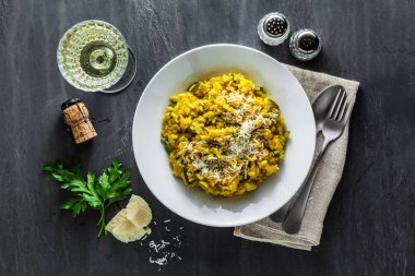 İtalyan yemek sarı Risotto milanese safran, kabak ve Parmesan peyniri bir bardak beyaz şarap bir siyah arduvaz masada. Kuzey İtalya mutfak