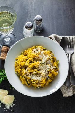 İtalyan yemek sarı Risotto milanese safran, kabak ve Parmesan peyniri bir bardak beyaz şarap bir siyah arduvaz masada. Kuzey İtalya mutfak