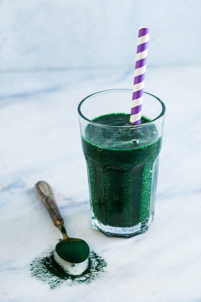 a tall glass of green fruit smoothie with Hawaiian spirulina on a marble table. healthy full breakfast