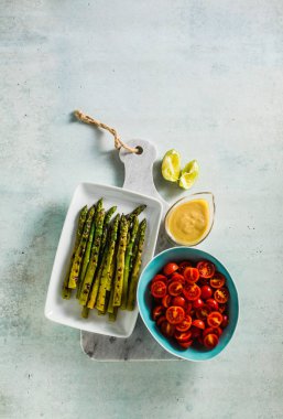  yeşil sağlıklı malzemelerle ızgara kuşkonmaz, cherry domates, tahin ve sosu bir mermer kesme tahtası üzerinde kireç 