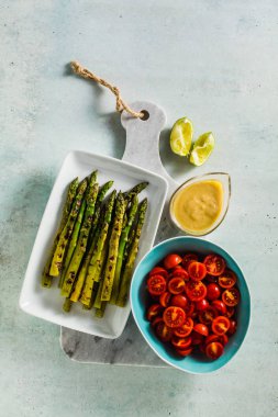  yeşil sağlıklı malzemelerle ızgara kuşkonmaz, cherry domates, tahin ve sosu bir mermer kesme tahtası üzerinde kireç 