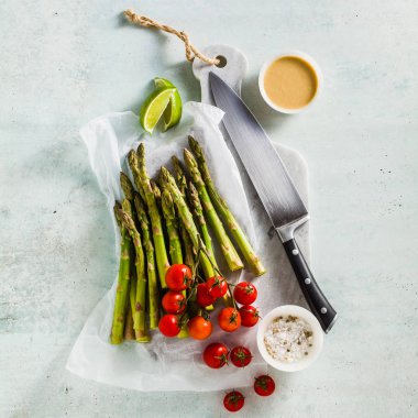 yeşil kuşkonmaz, cherry domates, tahin ve limon sosu bir mermer kesme tahtası ve bir şefin bıçak taze sağlıklı malzemelerle