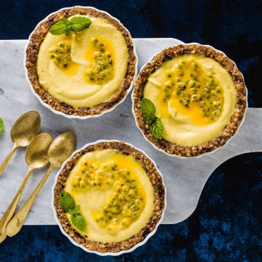 Vegan ham mini fındık ve tarihleri kireç suyu ve tutku meyve tohumları ile saf kaju-mango kremalı tart. beyaz mermer zemin üzerinde sağlıklı alternatif gıda