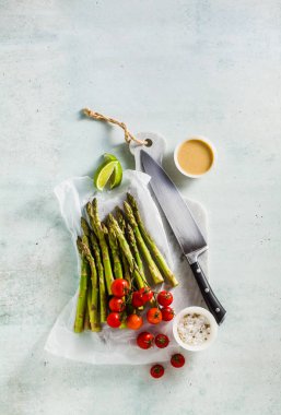 yeşil kuşkonmaz, cherry domates, tahin ve limon sosu bir mermer kesme tahtası ve bir şefin bıçak taze sağlıklı malzemelerle