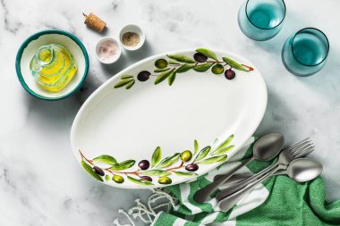 Zeytin ağacı dalları beyaz mermer masada boş el yapımı oval tabak. zeytinyağı ve çatal bıçak takımı. Akdeniz tablo ayarı