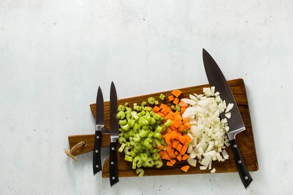 a set of knives on a wooden cutting board and chopped vegetables