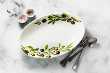 Zeytin ağacı dalları beyaz mermer masada boş el yapımı oval tabak. zeytinyağı ve çatal bıçak takımı. Akdeniz tablo ayarı