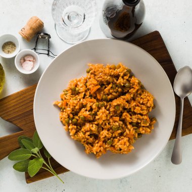 İtalyan risotto ile domates sosu ve yeşil bezelye, ahşap kesme tahtası ve bir şişe köpüklü şarap tabakta servis. klasik Akdeniz mutfağı. Tüm aile için sağlıklı vegan yemek