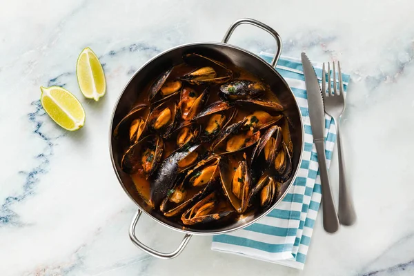 freshly cooked mussels in a frying pan in tomato sauce. pepata di cozze or mussels marinara. classic dish of mediterranean italian cuisine on white with blue marble table