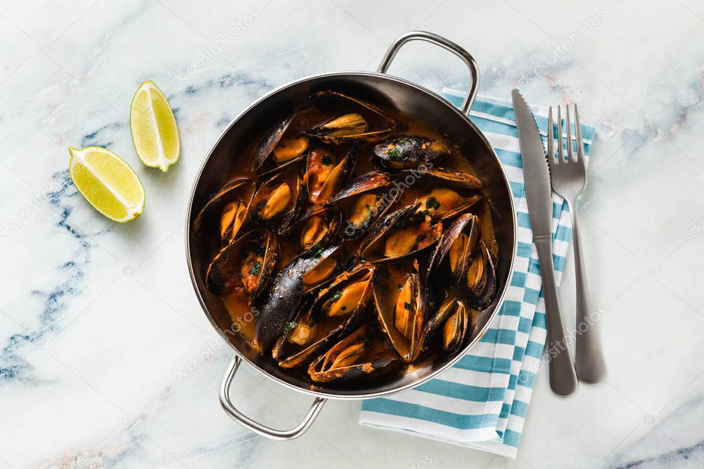 freshly cooked mussels in a frying pan in tomato sauce. pepata di cozze or mussels marinara. classic dish of mediterranean italian cuisine on white with blue marble table