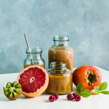 farklı gözlük ile taze greyfurt, kivi, Trabzon hurması ve ahududu smoothies yaptı. beyaz masa ve mavi arka plan. sağlıklı gıda. sabah kahvaltı