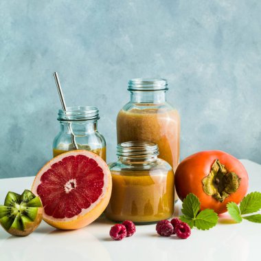 farklı gözlük ile taze greyfurt, kivi, Trabzon hurması ve ahududu smoothies yaptı. beyaz masa ve mavi arka plan. sağlıklı gıda. sabah kahvaltı