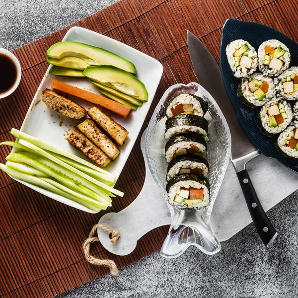 vegan ready-made sushi on the table in fish plates. rolls with fried tofu, cucumber, boiled carrots and fresh avocado. healthy vegan food