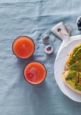 Roka ve avokado sandviç masada kırmızı biber ile. Sağlıklı Kahvaltı veya aperatif bir mavi keten masa örtüsü ve taze sıkılmış greyfurt suyu bir plaka üzerinde