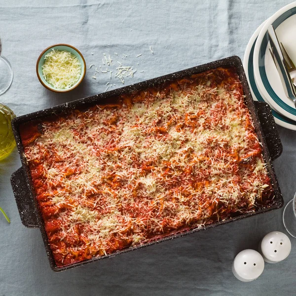 vegan lasagna with lentils and green peas in a baking sheet on a table with a blue linen tablecloth. healthy Italian cuisine for the whole family, party or restaurant and red wine in glasses