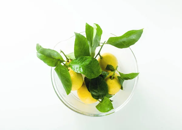 Några färska mogna citroner med löv i en stor glasskål på — Stockfoto