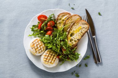 grilled Italian Tomino cheese served on a table with arugula sal clipart
