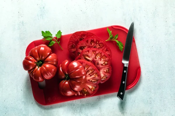 Fleischtomaten in Scheiben geschnitten auf einem roten Schneidebrett und einem Messer. Koch — Stockfoto