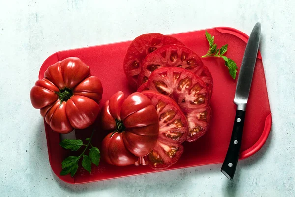 Fleischtomaten in Scheiben geschnitten auf einem roten Schneidebrett und einem Messer. Koch — Stockfoto