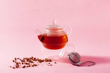 Pembe arka planda cam çaydanlıkta çay ve metal Infuser Filtresi