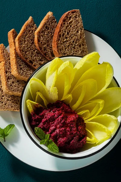 vegan snack of spread of roasted beets and pistachios and leaves of Belgian Endive with whole grain bread on the table