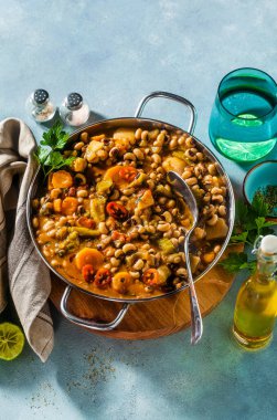 Siyah gözlü Pea Vegan Chili metal bir tavada ahşap bir stantta mavi bir arka planda