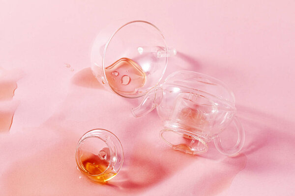 thrown glass teapot and spilled tea on a pink background. abstract
