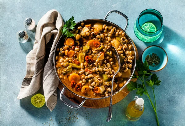 Siyah gözlü Pea Vegan Chili metal bir tavada ahşap bir stantta mavi bir arka planda
