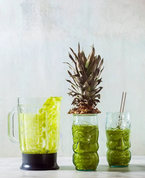 Freshly prepared green pineapple smoothie in glasses with faces and bowl of glass blender . Healthy morning breakfast concept.