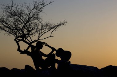 Günbatımının arka planında gitarlı bir adamın silueti.