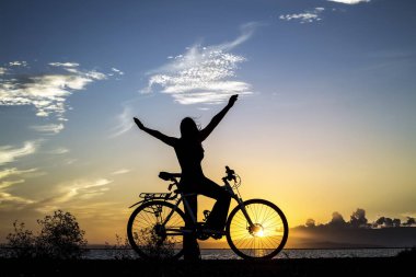 Sahilde bisikleti olan genç bir kadının silueti.