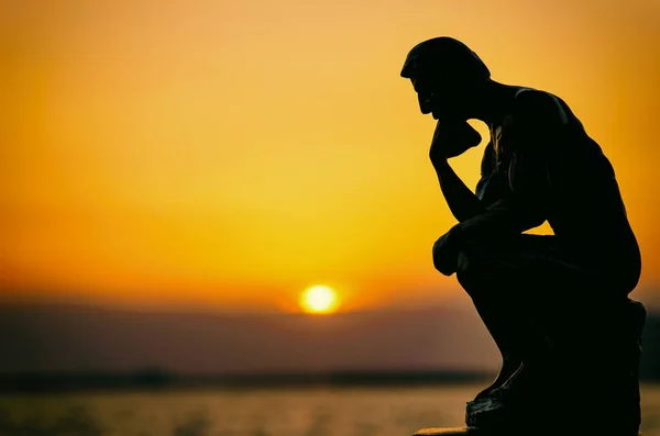 A person thinks by the sea at sunset