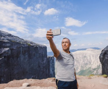 Norveç, selfie, özgürlük elinde tutan bir smartphone dağlar kjeragbolten kjerag taştan yakışıklı yaşlı adam için bir aşırı planı seyahat portresi