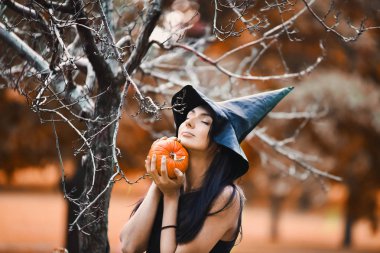 Turuncu kabak ile siyah şapkalı bir genç kız cadı yakın çekim el sarı sonbahar Bahçe park Halloween pumpkins ile kutluyor