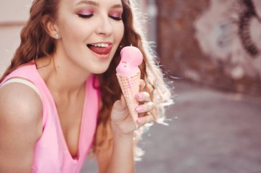 yakın çekim bir gözleme dondurma boynuz yalıyor tutan pembe elbise ve yaşam tarzı gülümseyen puffs kıvırcık saçlı Genç güzel seksi kız portresi
