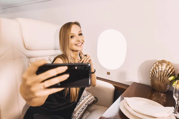 beautiful young girl in the cabin of a business class airplane with a phone in her hands comfortable luxury travel